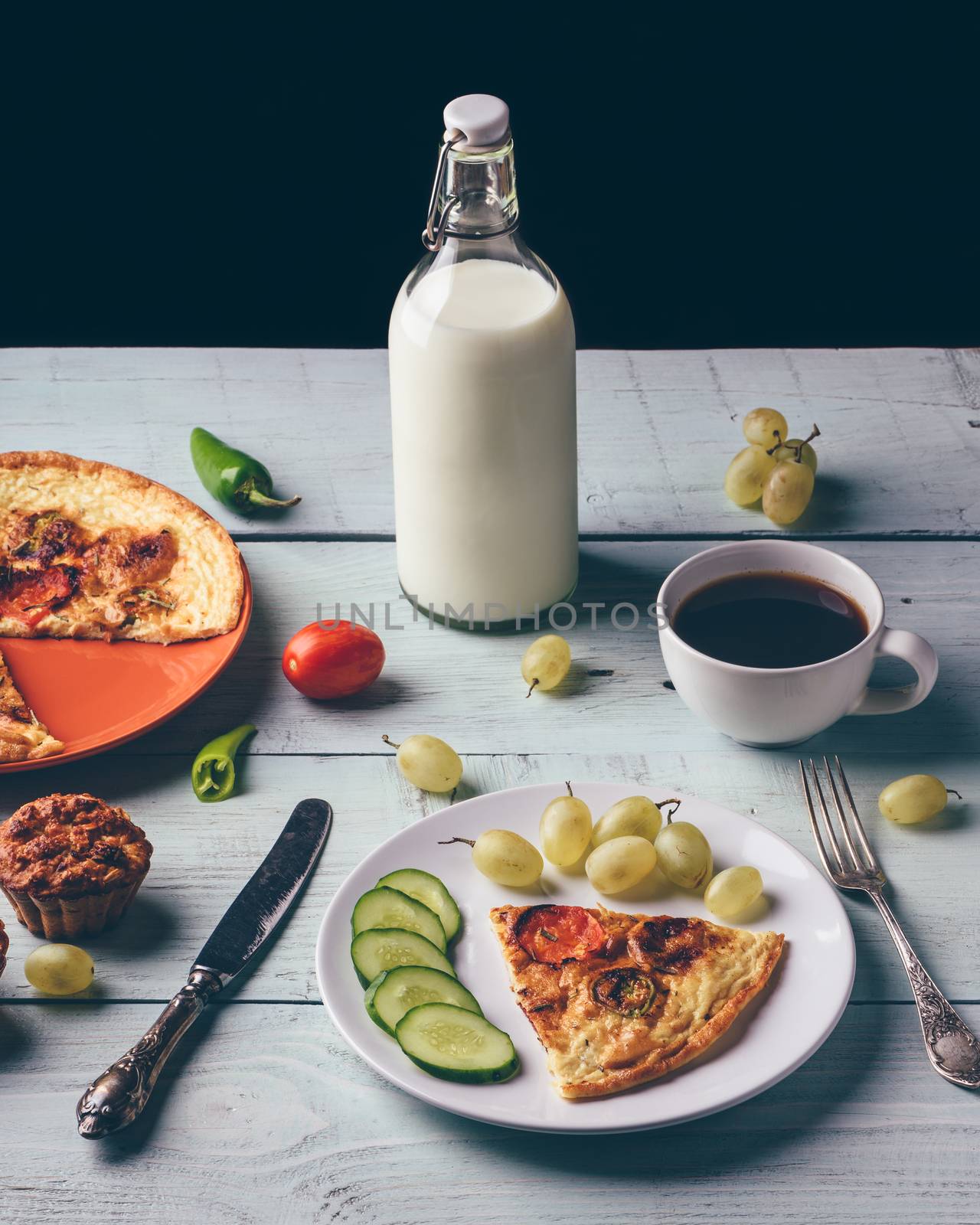 Healthy breakfast with frittata, fruits, vegetables, milk, cup of coffee and muffins on light wooden background.