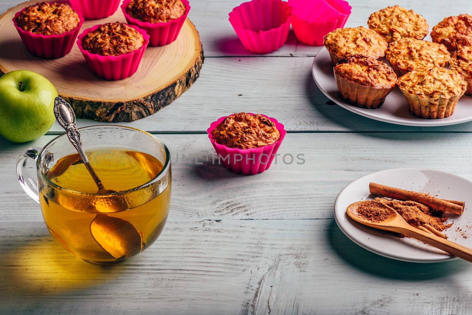 Healthy Breakfast. Cooked oatmeal muffins with apple and cup of green tea over light wooden background.