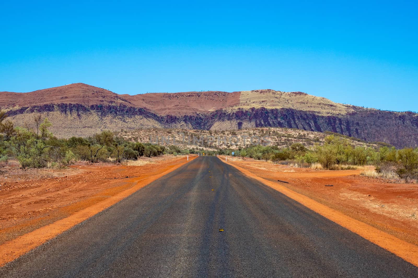 Unmarked freshly paved road leading straight towards mountain wall at Karijini National Park by MXW_Stock