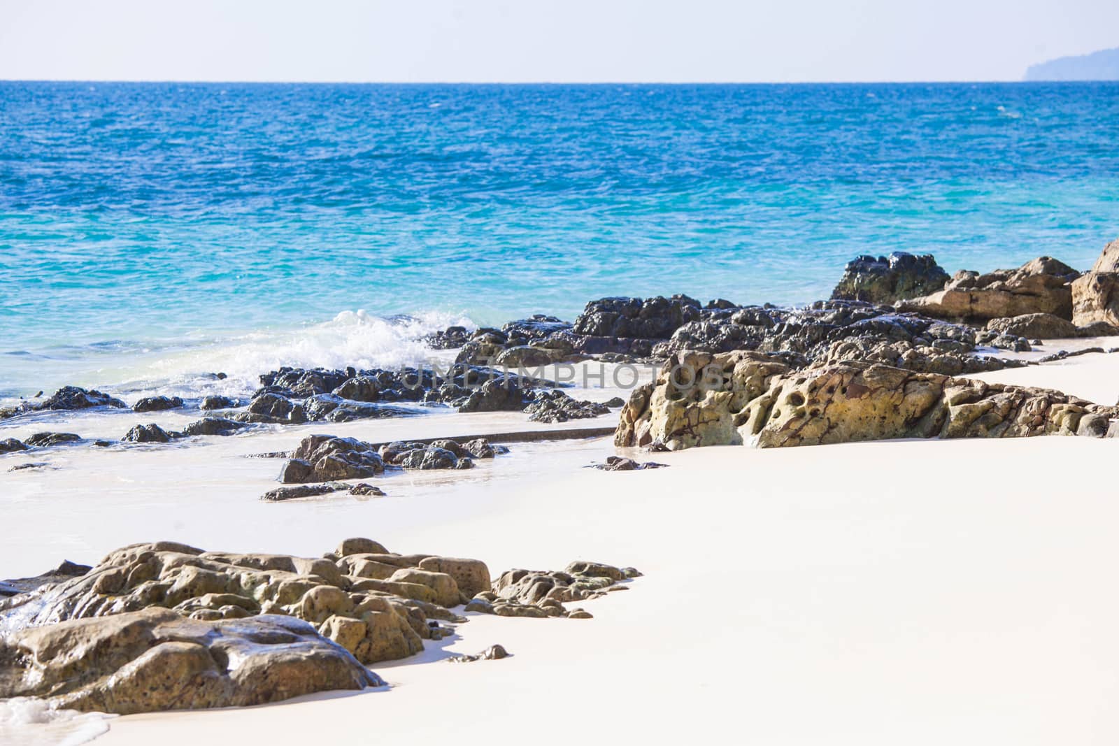 White fine sand coral beach with stones and blue tropical sea in Thailand