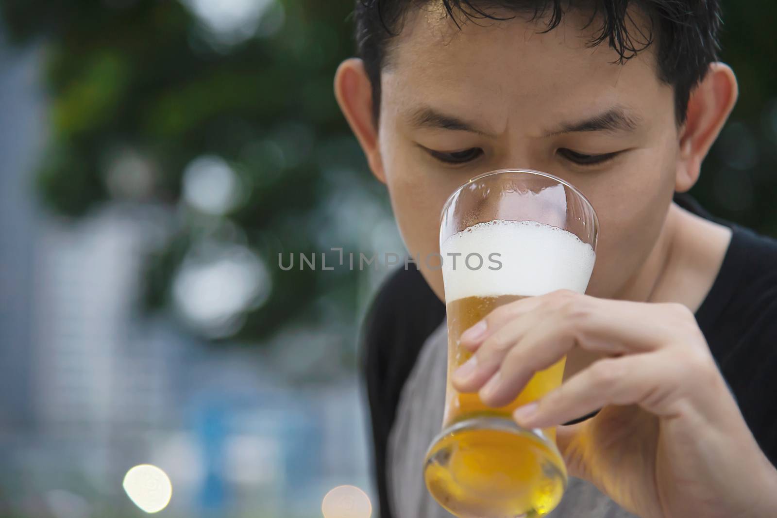 Asian man drinking beer in green garden restaurant - people relax enjoy soft drink lifestyle concept