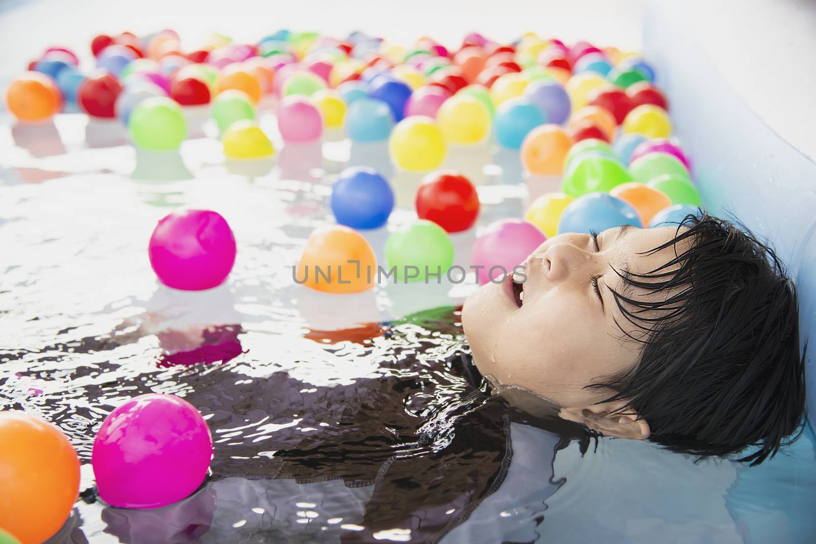 Boy playing with colourful ball in small swimming pool toy - happy boy in water pool toy concept