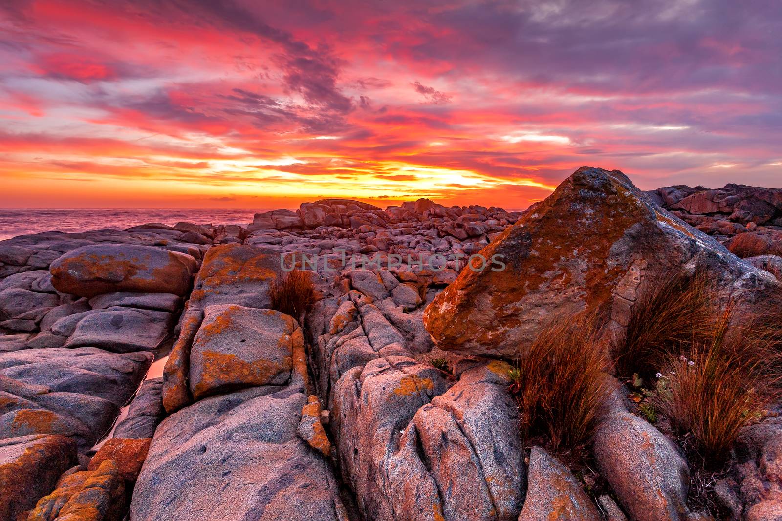 Rich blazing red orange and yellow vivid colour sunrise over the ocean and rocky coastal landscape.  Australia
