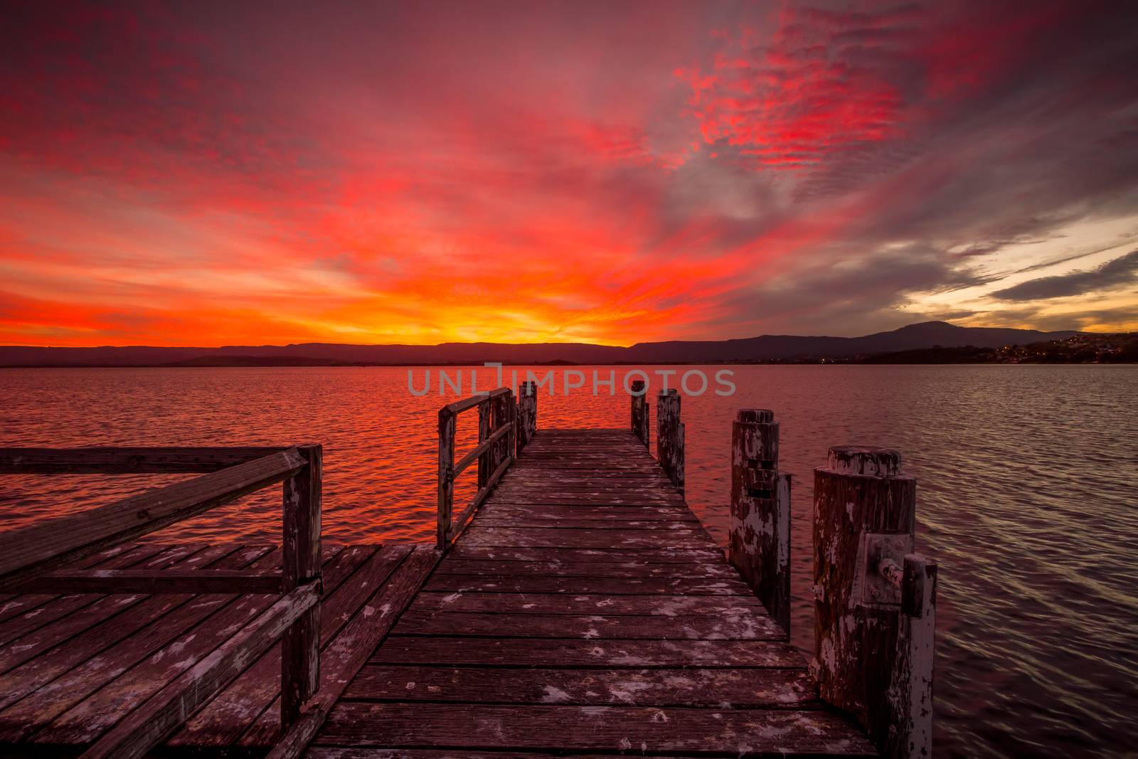 Burning red fiery sunset across Lake Illawarra with rustic timber jetty