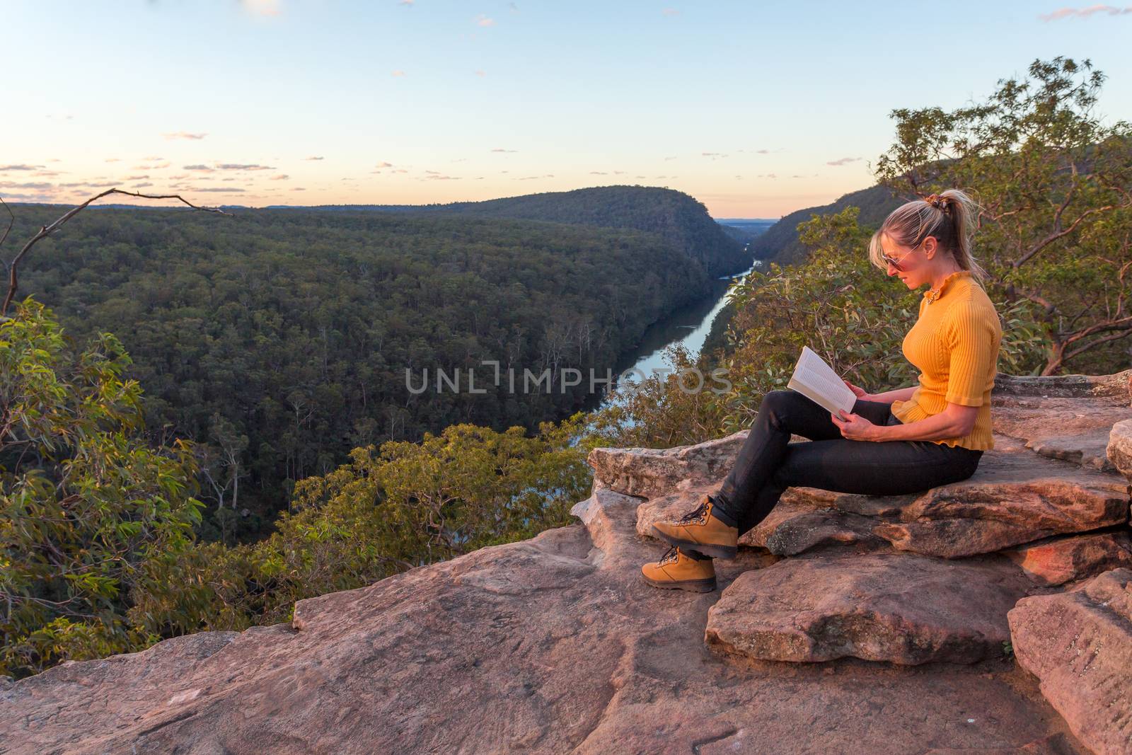 A woman sitting on a rock reading in nature by lovleah