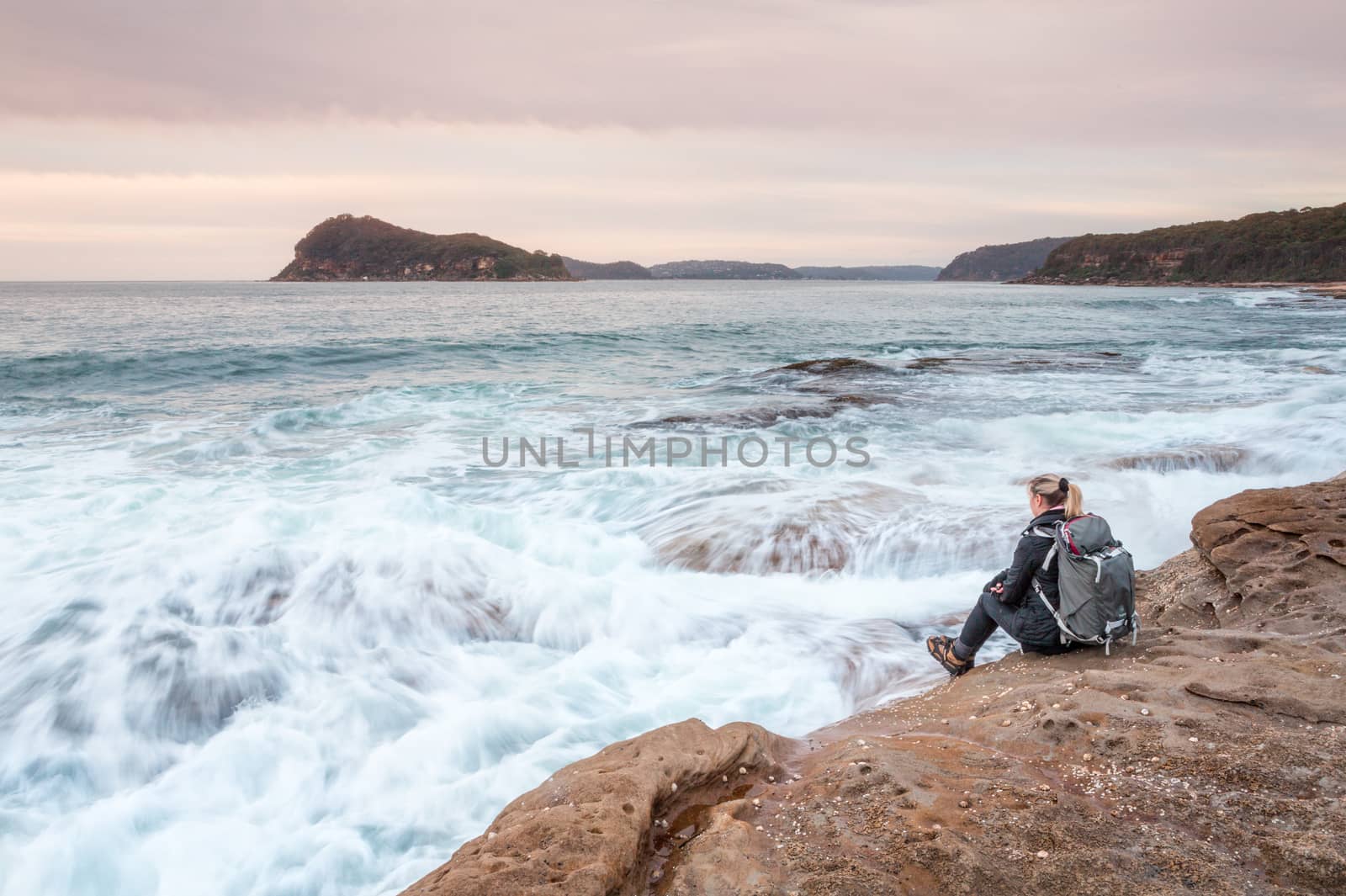 Woman sitting by the ocean letting waves lap at her feet by lovleah