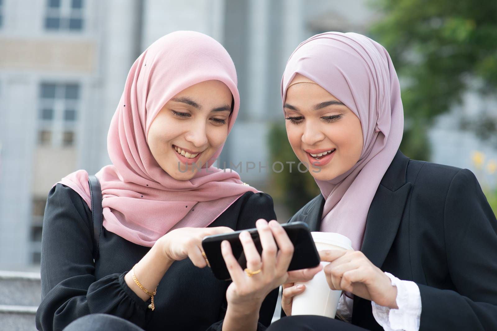 Muslim women using smart phone, sharing and laughing.