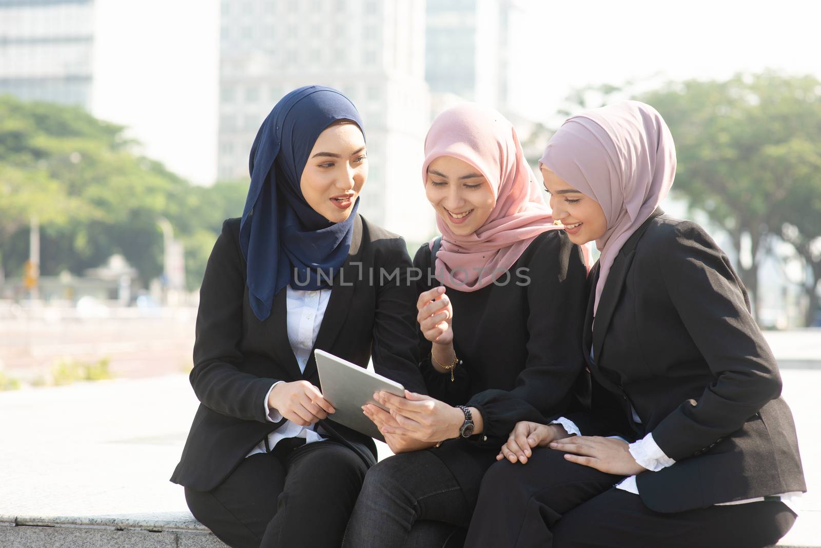 Group of Muslim business women discussing, using tablet pc outdoor.