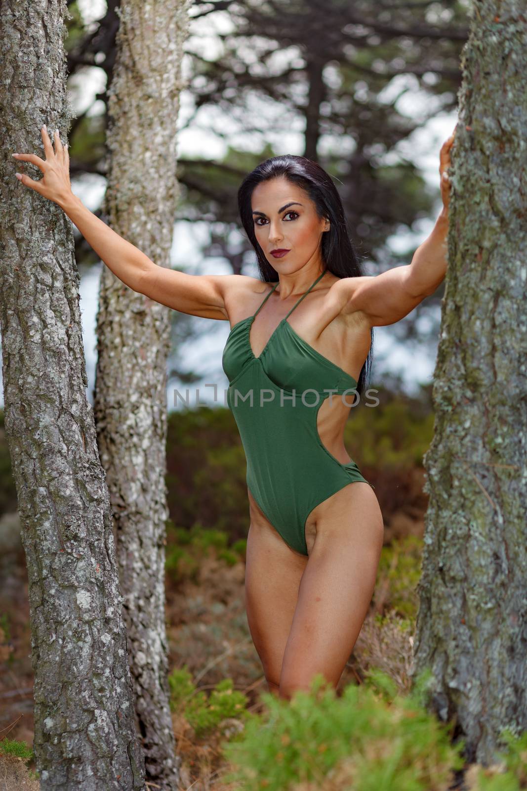 Fitness girl posing in the beach forest between 
trees  with a beautiful green swimsuit