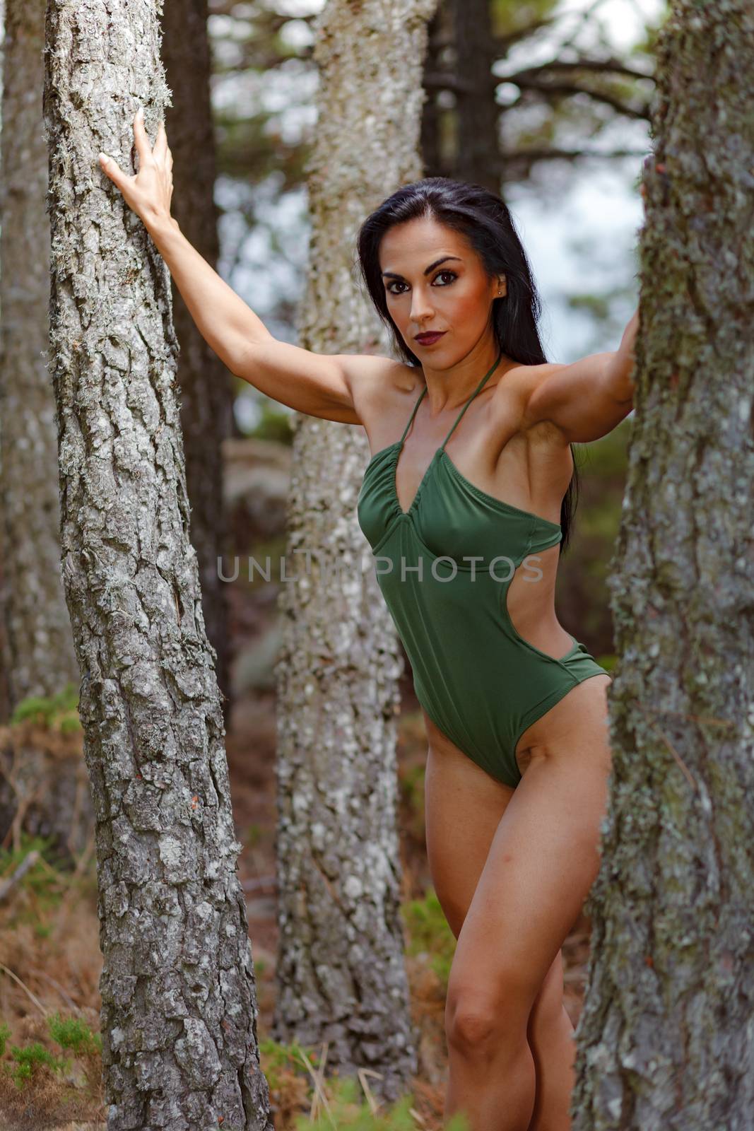 Fitness girl posing in the beach forest between 
trees  with a beautiful green swimsuit