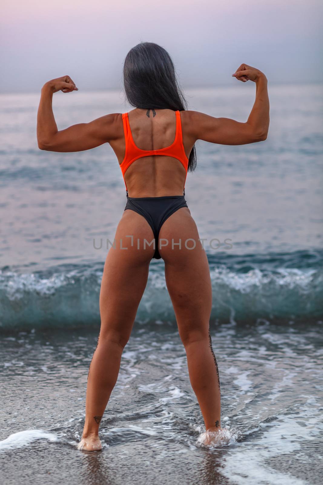 Fitness girl posing 
in the shore of the beach with a beautiful black and orange bikini and sunglasses