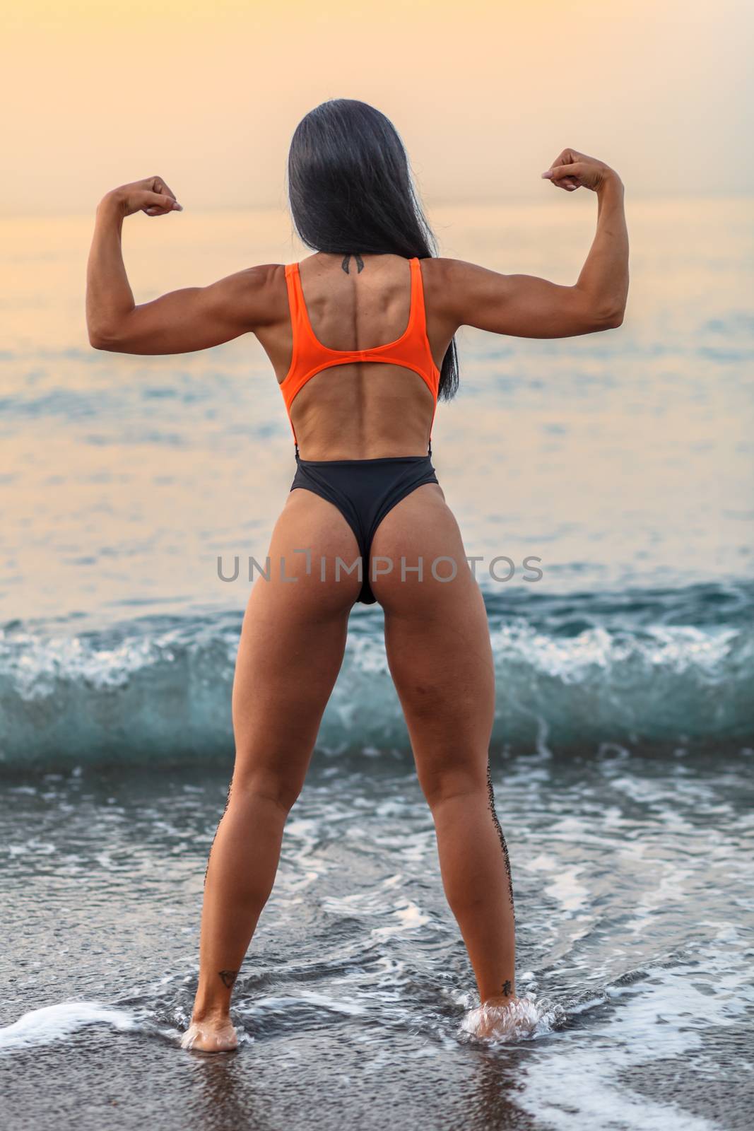 Fitness girl posing 
in the shore of the beach with a beautiful black and orange bikini and sunglasses