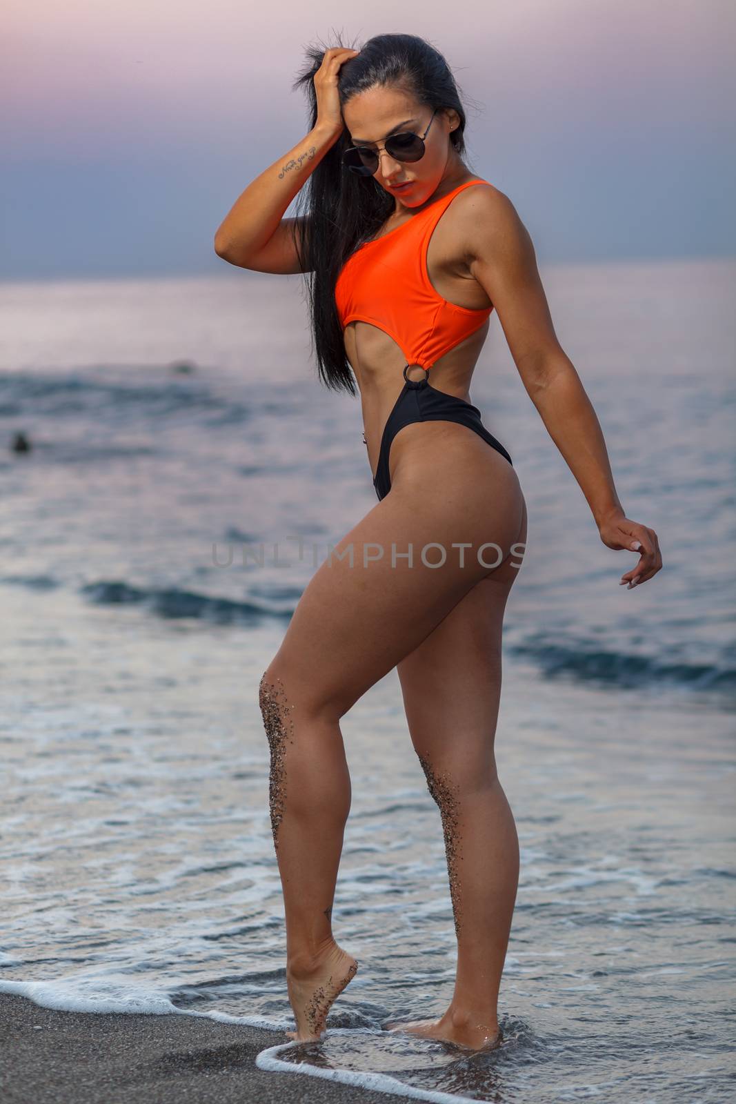 Fitness girl posing 
in the shore of the beach with a beautiful black and orange bikini and sunglasses