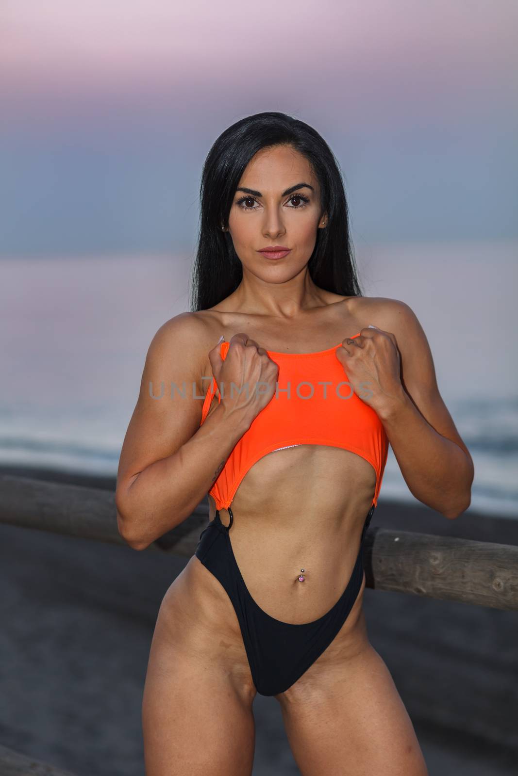 Fitness girl posing 
in the shore of the beach with a beautiful black and orange bikini