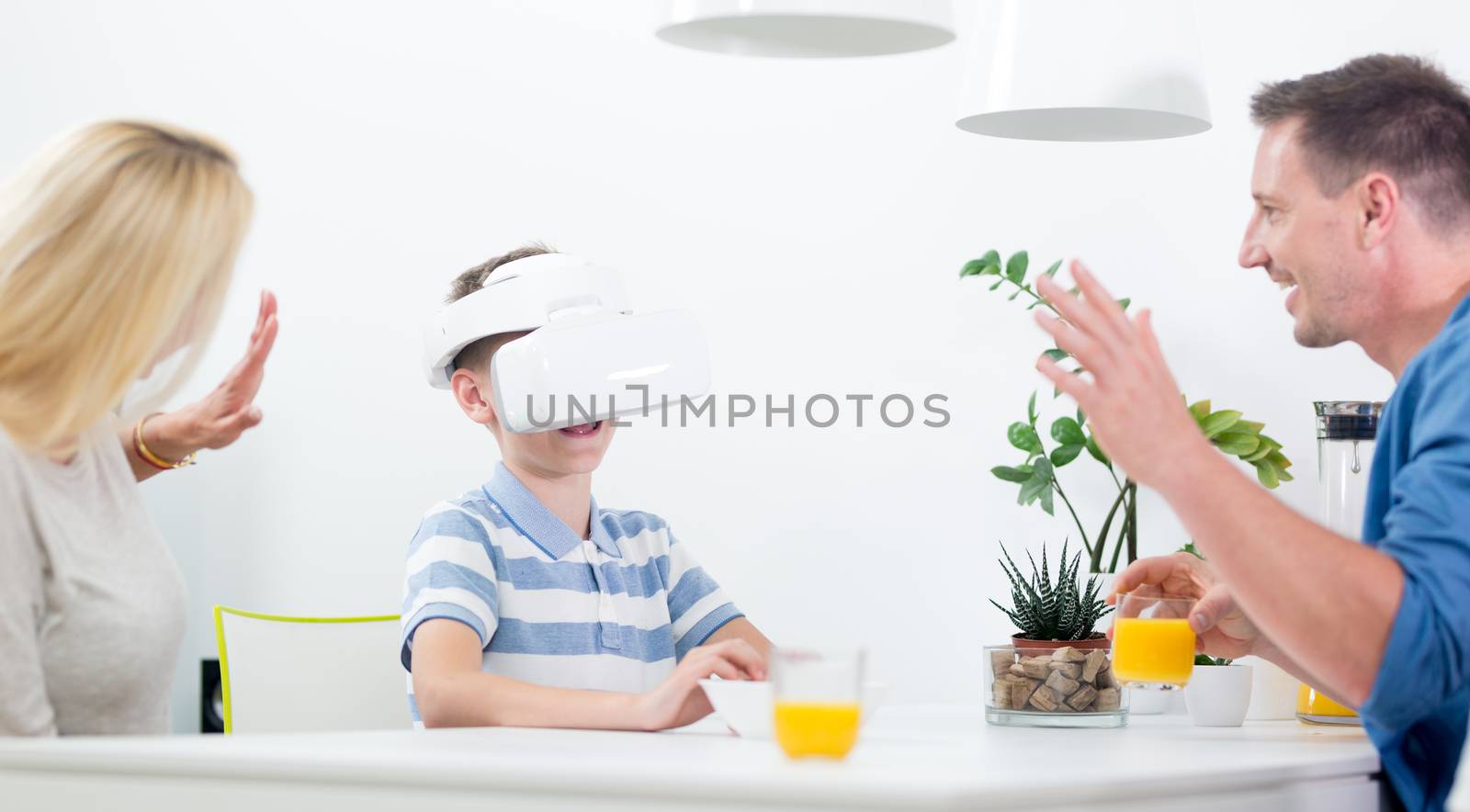 Happy caucasian family at home at dinning table, having fun playing games using virtual reality headset.