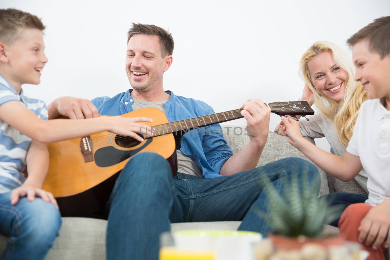 Happy caucasian family smiling while playing guitar and singing songs together at cosy modern home. Spending quality leisure time with children and family concept.