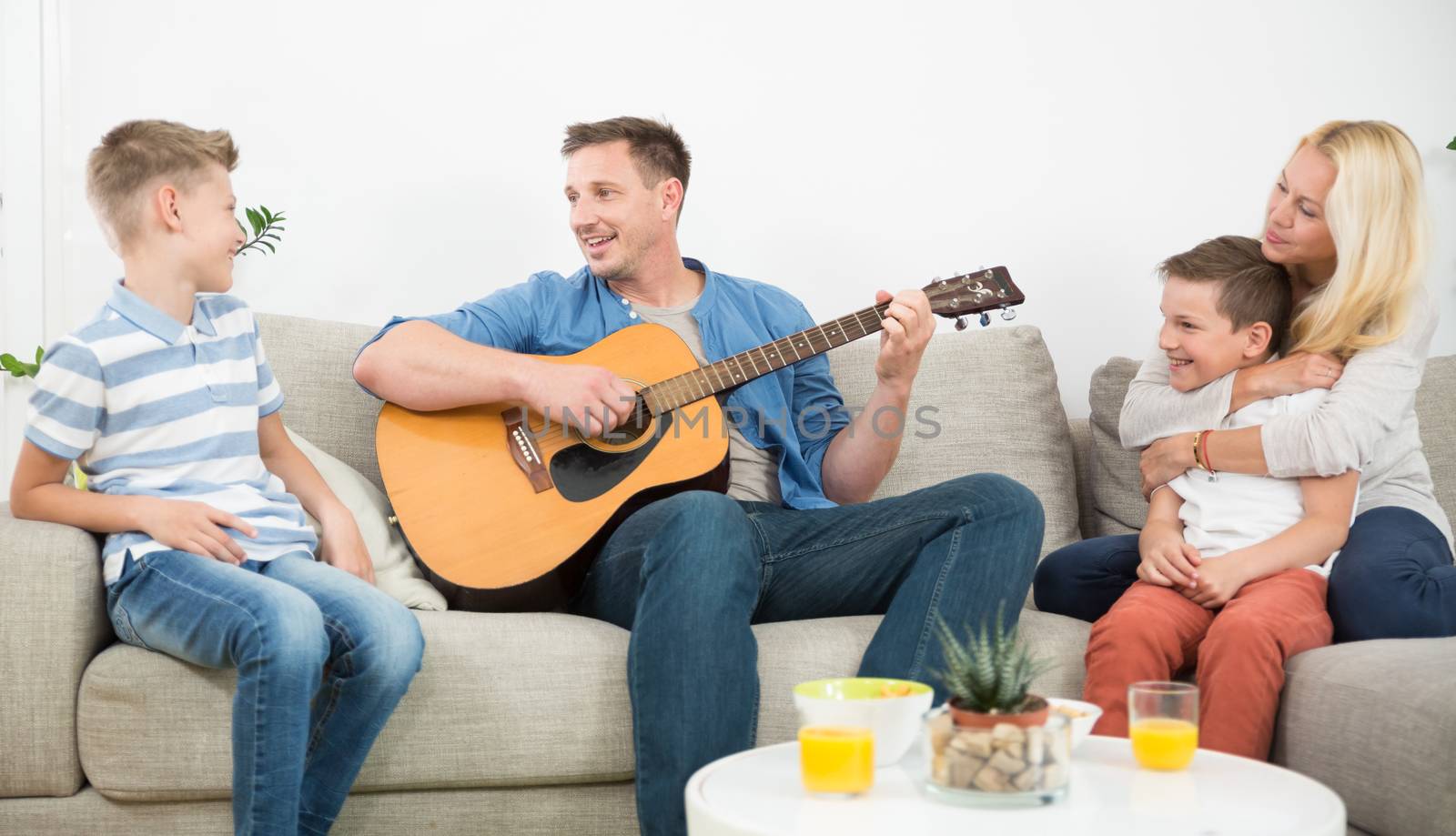 Happy caucasian family smiling, playing guitar and singing songs together at cosy modern home by kasto