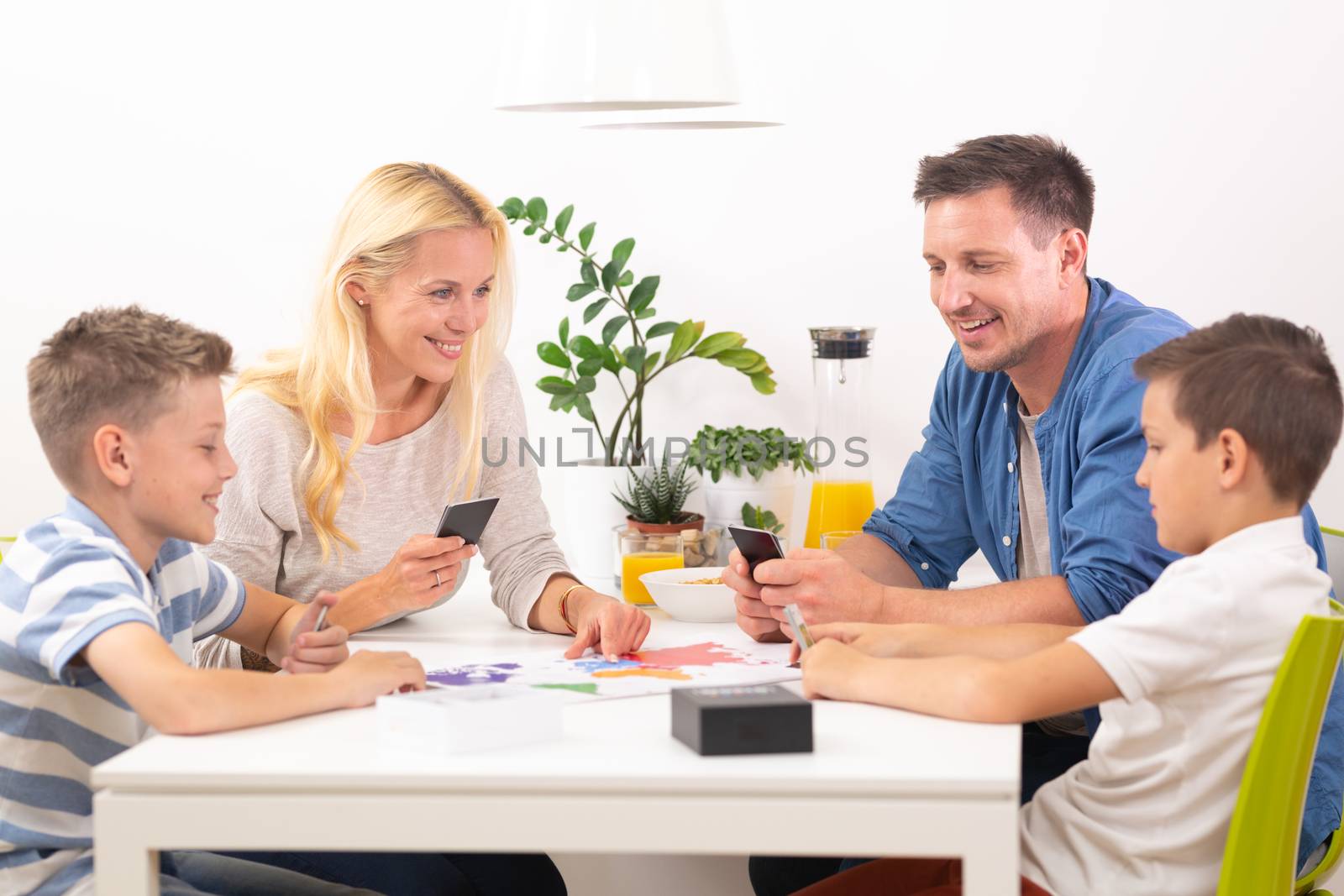 Happy young family playing card game at dining table at bright modern home. Spending quality leisure time with children and family concept. Cards are generic and debranded.