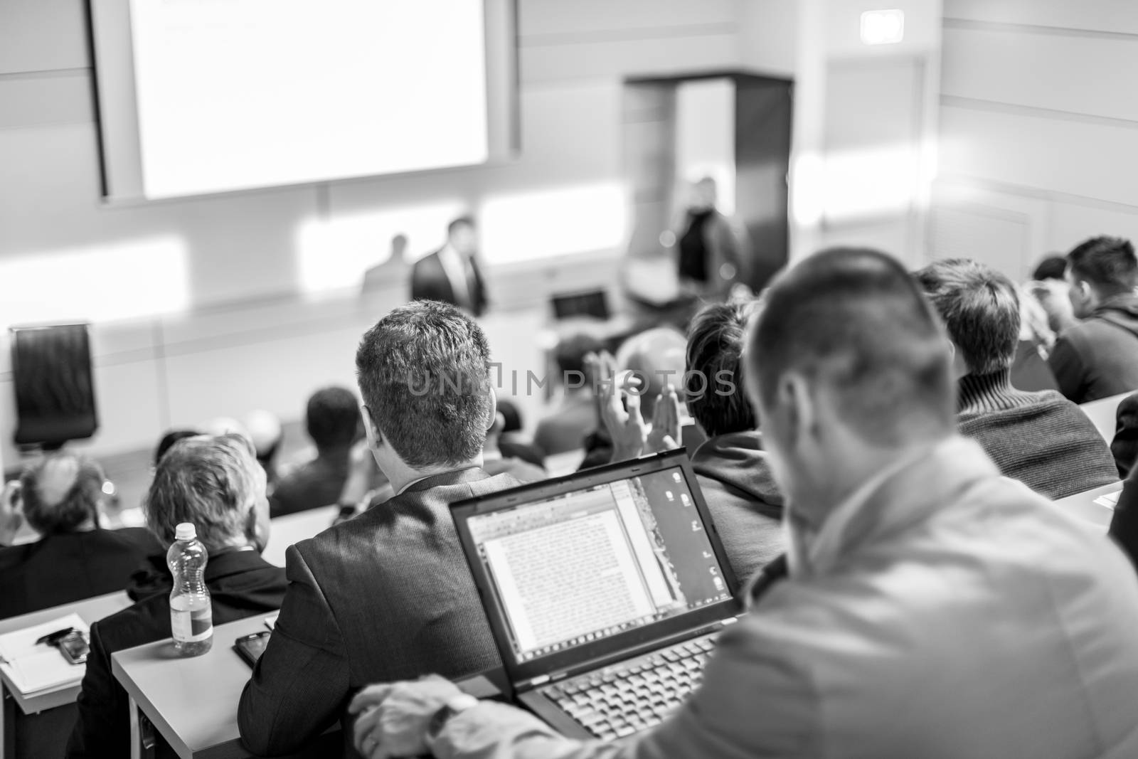 Speaker giving a talk in conference hall at business event. Audience at the conference hall. Business and Entrepreneurship concept. Focus on unrecognizable people in audience. Black and white.