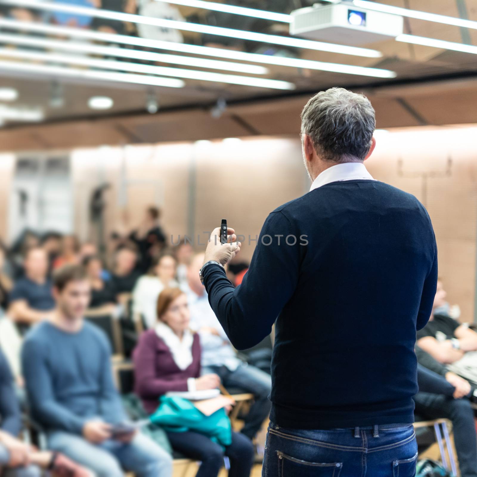 Expert giving a talk on business conference workshop. Unrecognizable people in audience at the conference hall. Business and entrepreneurship event.