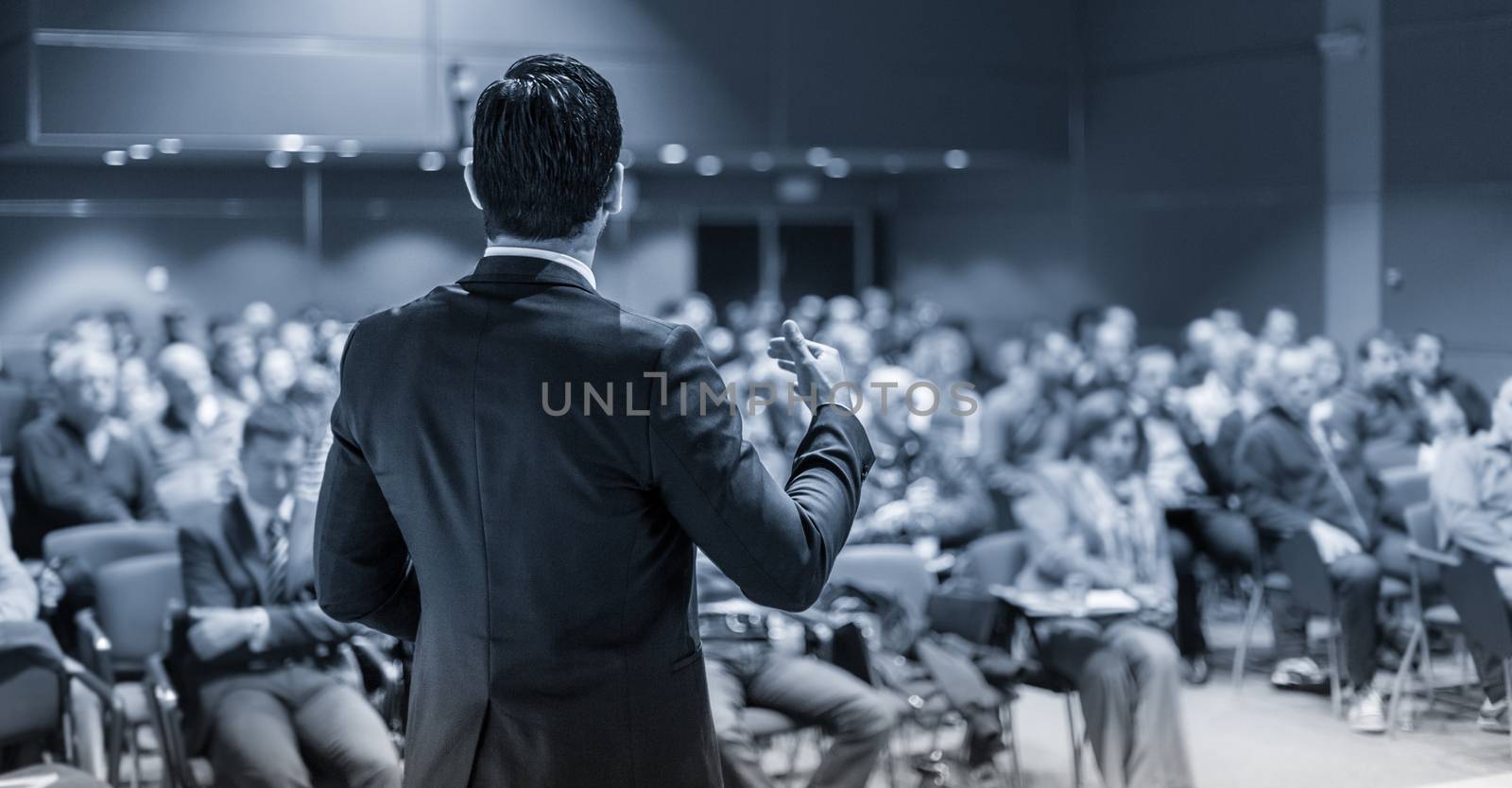 Speaker giving a talk on corporate business conference. Unrecognizable people in audience at conference hall. Business and Entrepreneurship event. Black and white image.