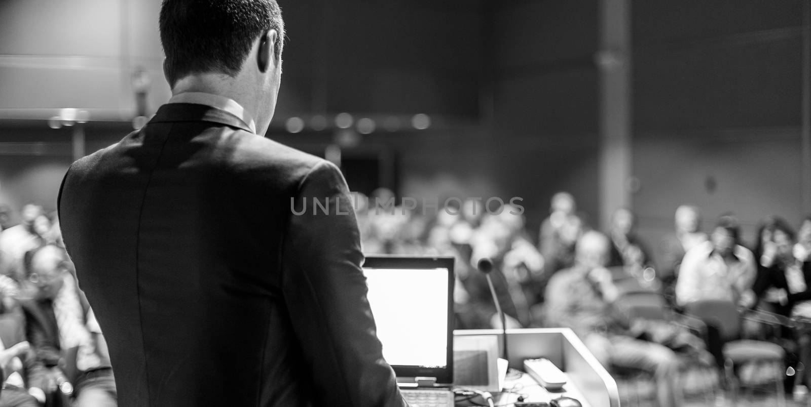 Speaker giving a talk on corporate business conference. Unrecognizable people in audience at conference hall. Business and Entrepreneurship event. Black and white image.