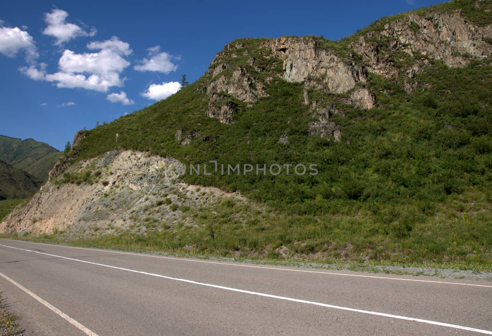 A fragment of an asphalt road at the foot of a rocky mountain. Chuysky tract, Altai, Siberia, Russia.