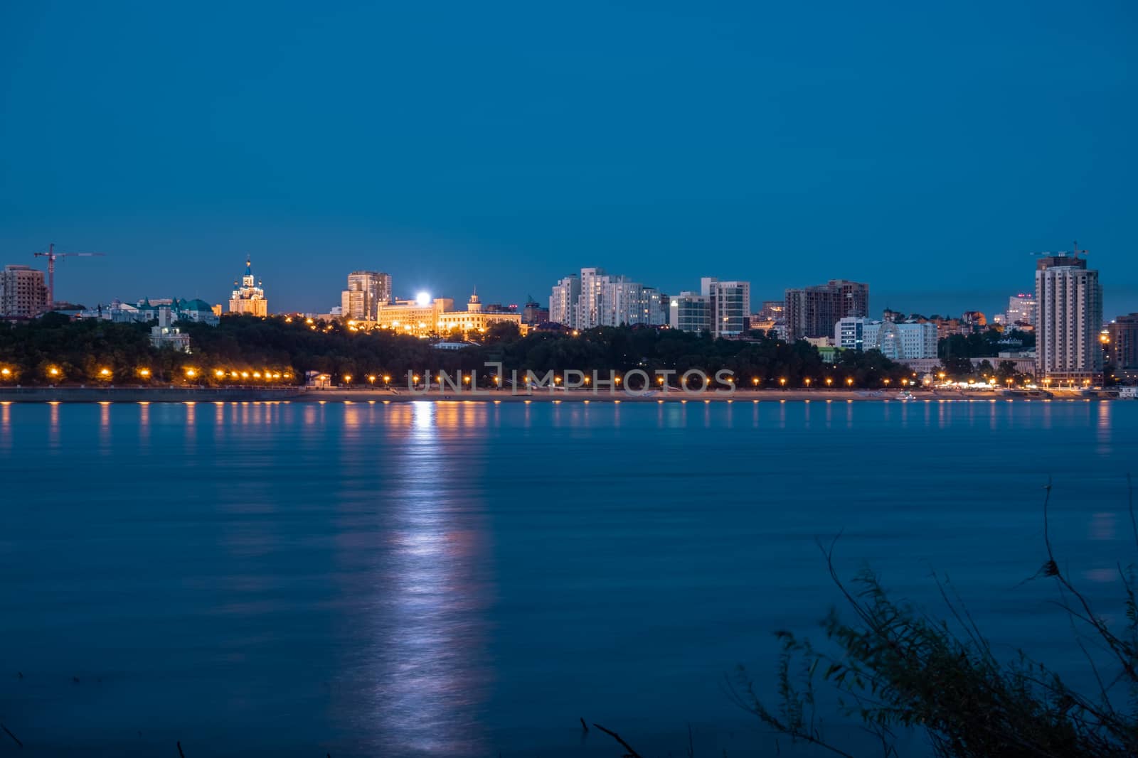 Night View of the city of Khabarovsk from the Amur river. Blue night sky. The night city is brightly lit with lanterns