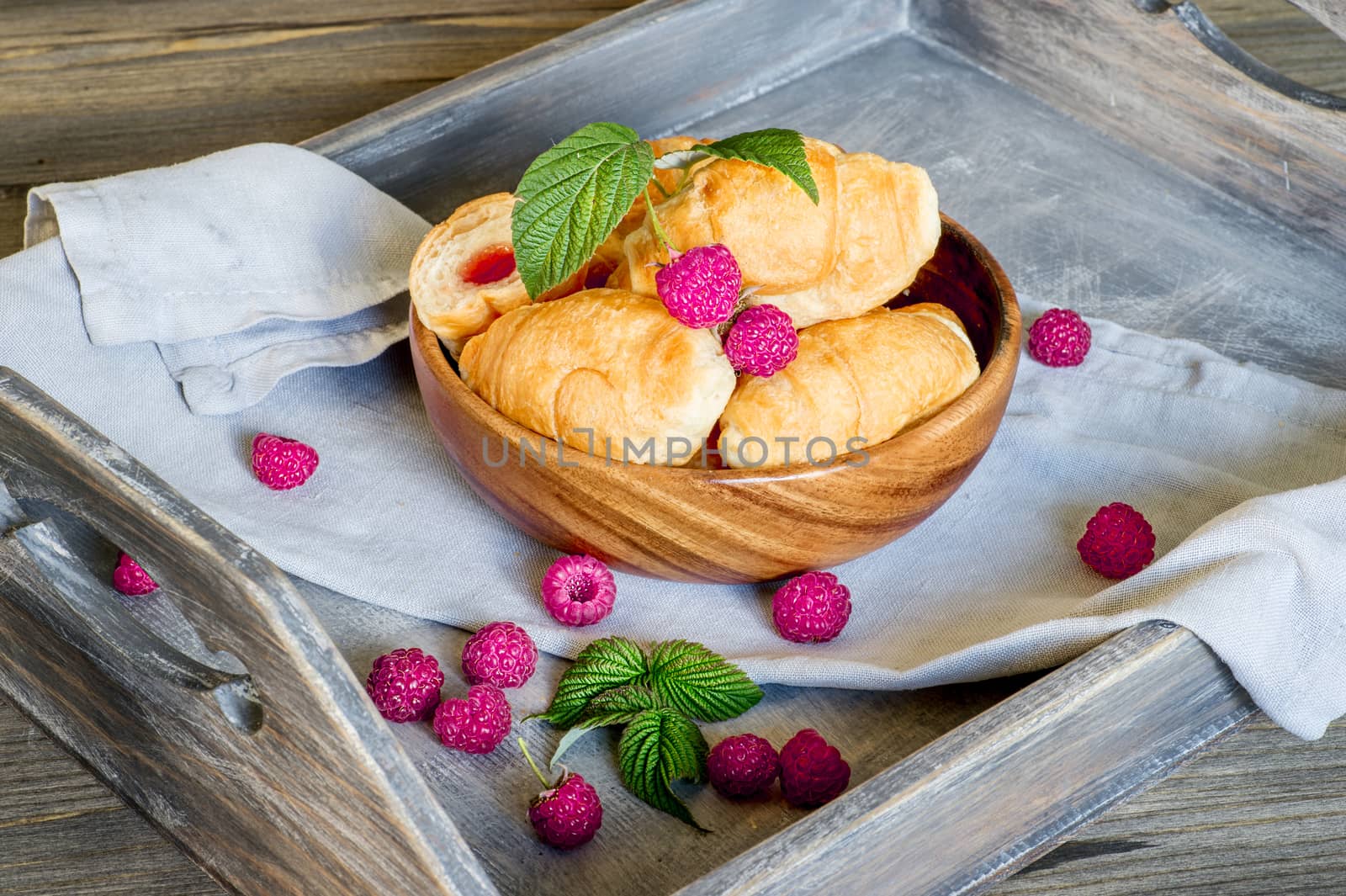 Croissants with raspberries on a wooden tray. The concept of a wholesome breakfast