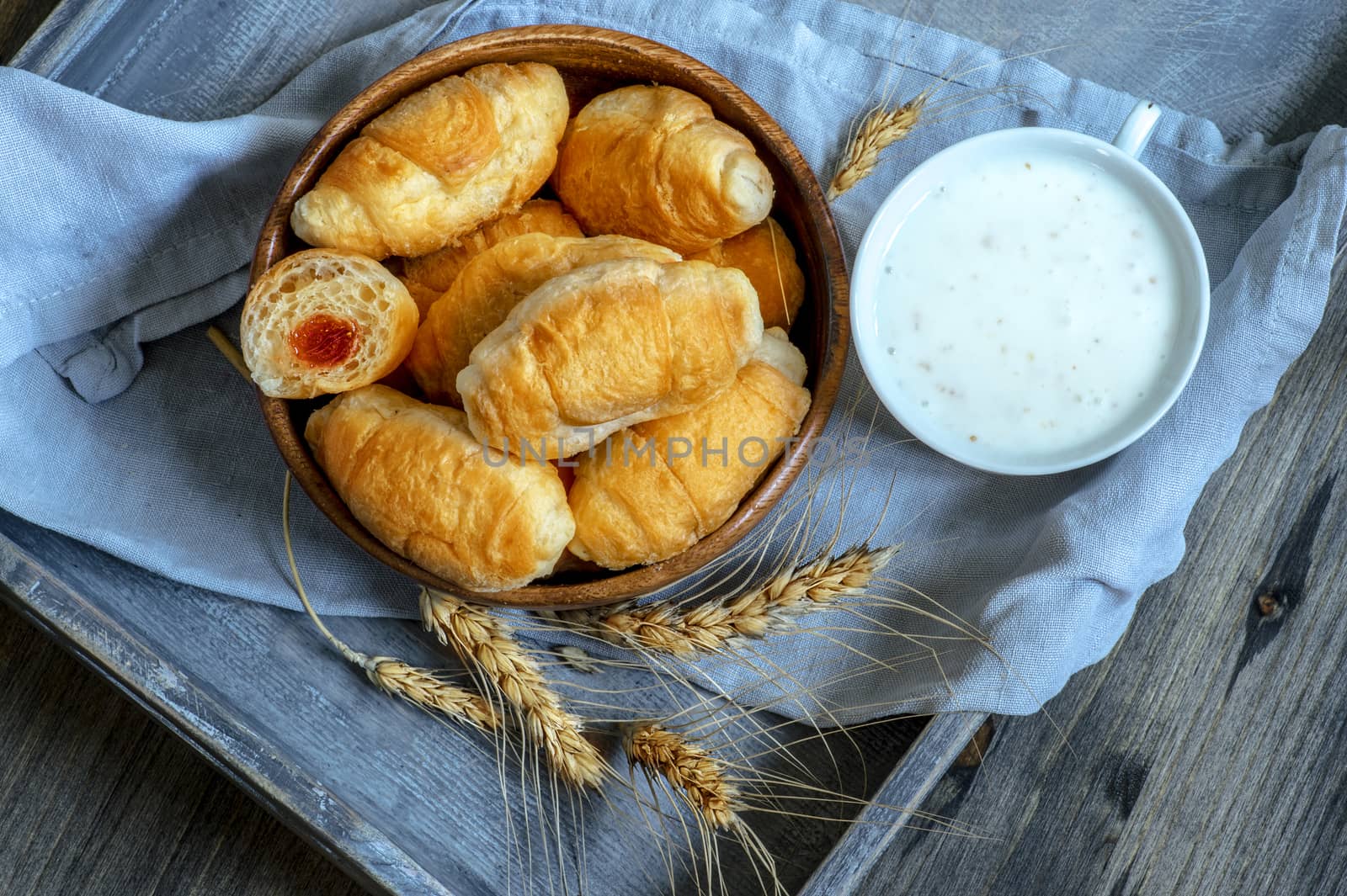 Croissants, a cup with kefir and ears of grain on a wooden tray. The concept of a wholesome breakfast