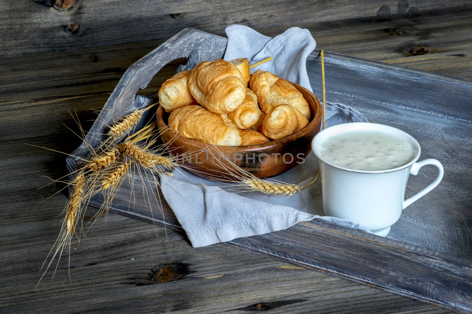 Croissants, a cup with kefir and ears of grain on a wooden tray. The concept of a wholesome breakfast