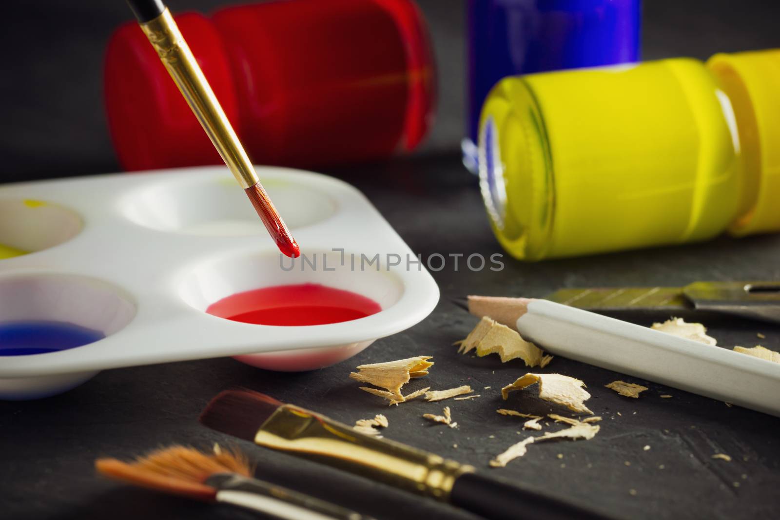 Closeup artist paint brush above color plate and poster color bottle on table. Concept of art education.