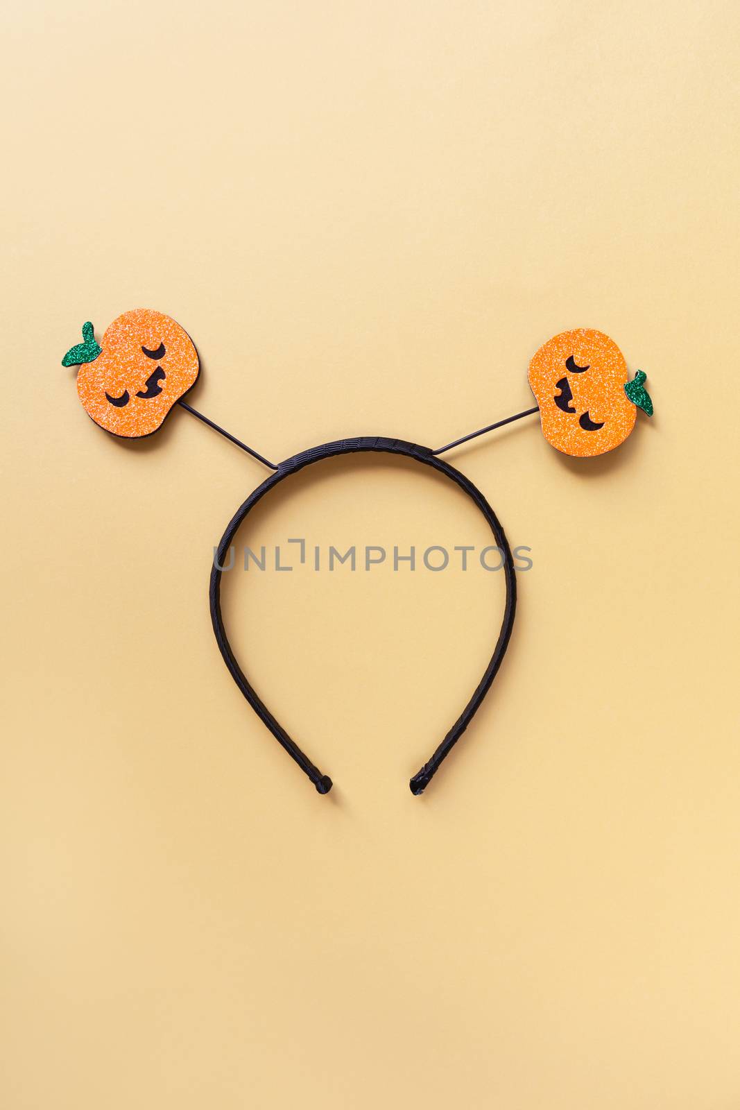 Halloween party accessory, rim with two shiny pumpkins with cute creepy faces. Pastel yellow background, central composition. Holiday flat lay. Minimal style. Vertical.