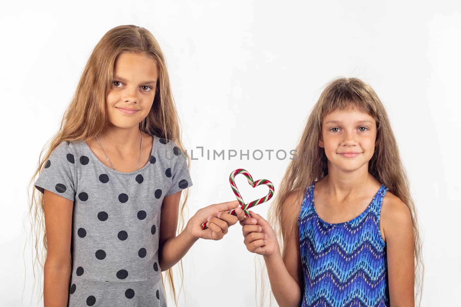 Two girls made a heart out of two lollipops and look into the frame