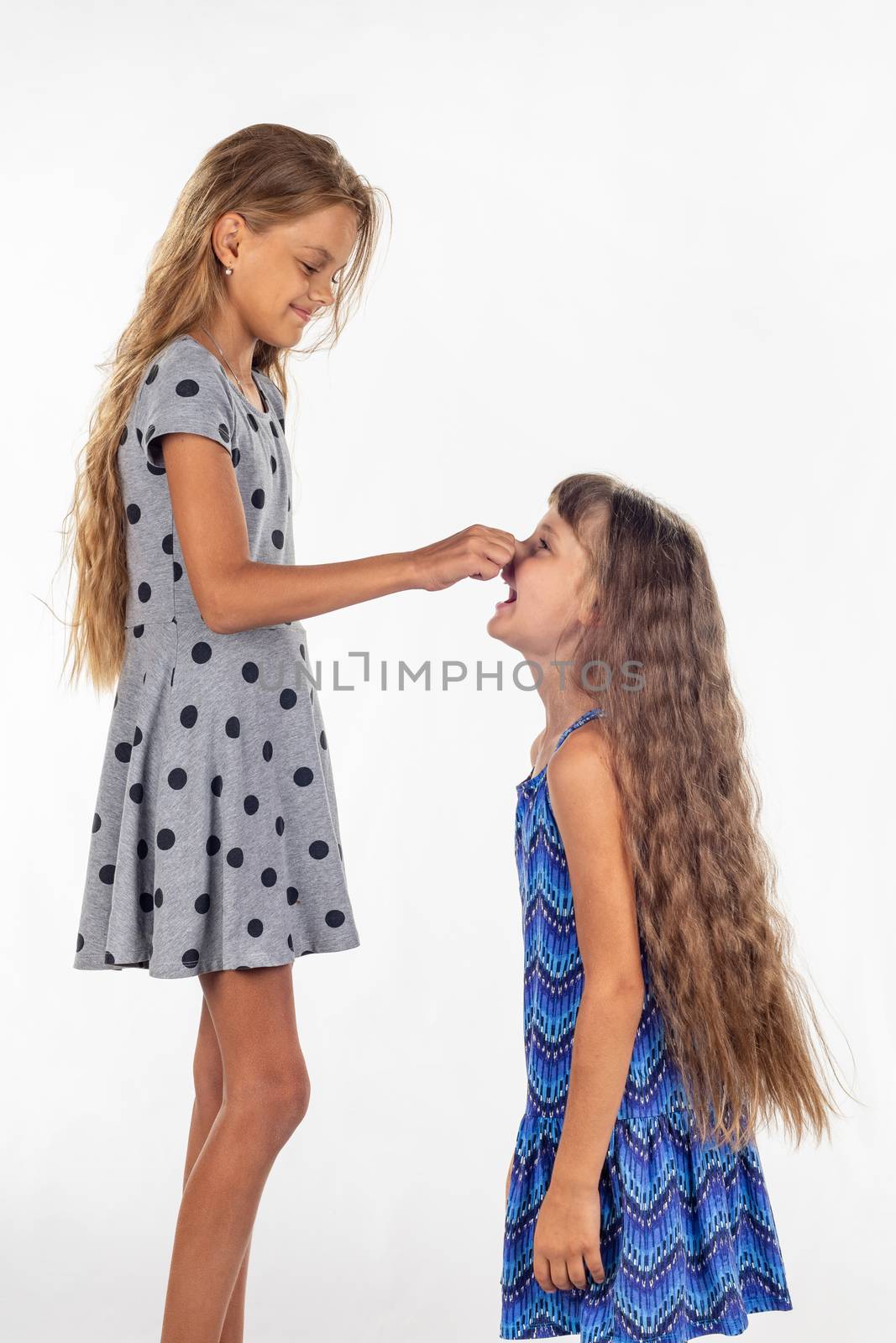 Two girls of different stature, one stood on a chair and pulls the other girl by the nose