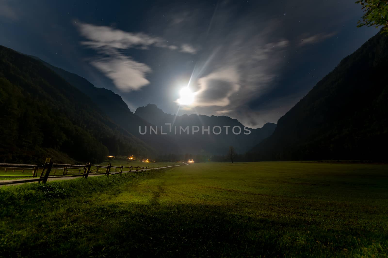 Alpine valley at night, landscape lit by full moon, stars visible, farmhouse with illuminated windows, mistyc and dreamy