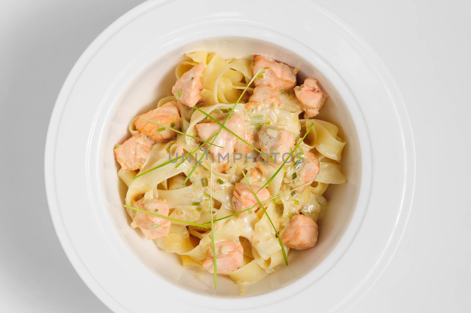 Fettuccine with salmon at white plate, top view