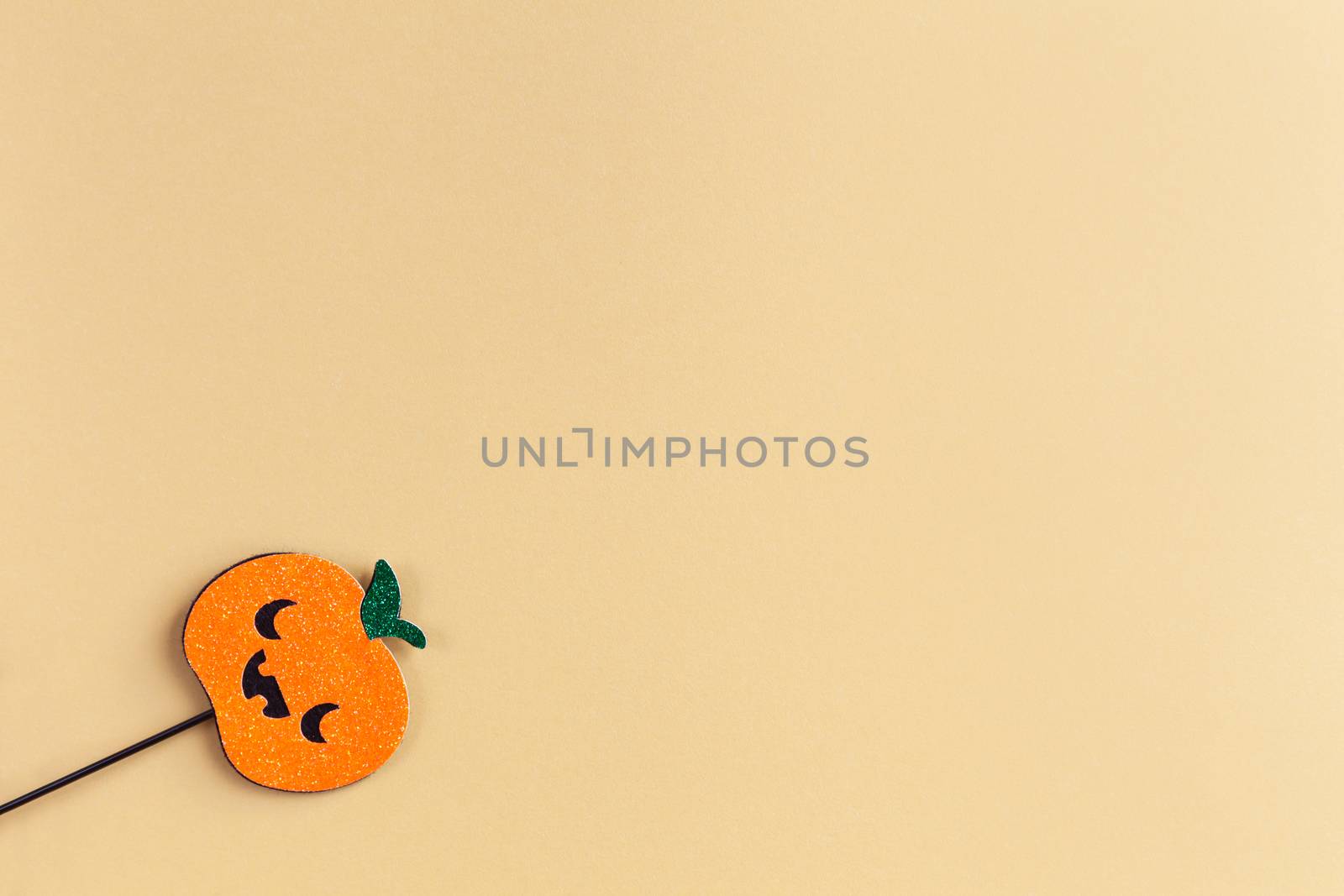 Halloween party accessory, shiny pumpkin with cute creepy faces. Pastel yellow background, place for text. Holiday flat lay. Minimal style. Horizontal.