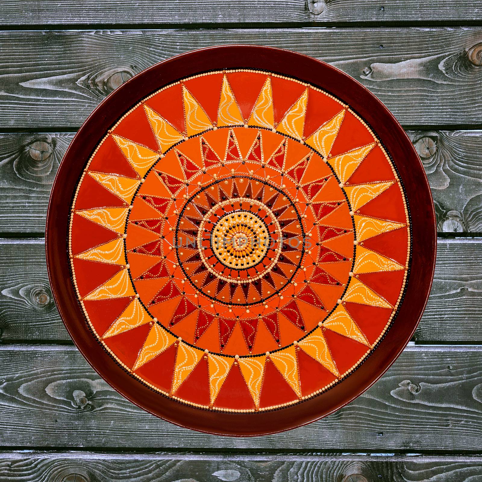 Decorative ceramic plate, hand painted dot pattern with acrylic paints on a gray wooden background. A square photo. Closeup