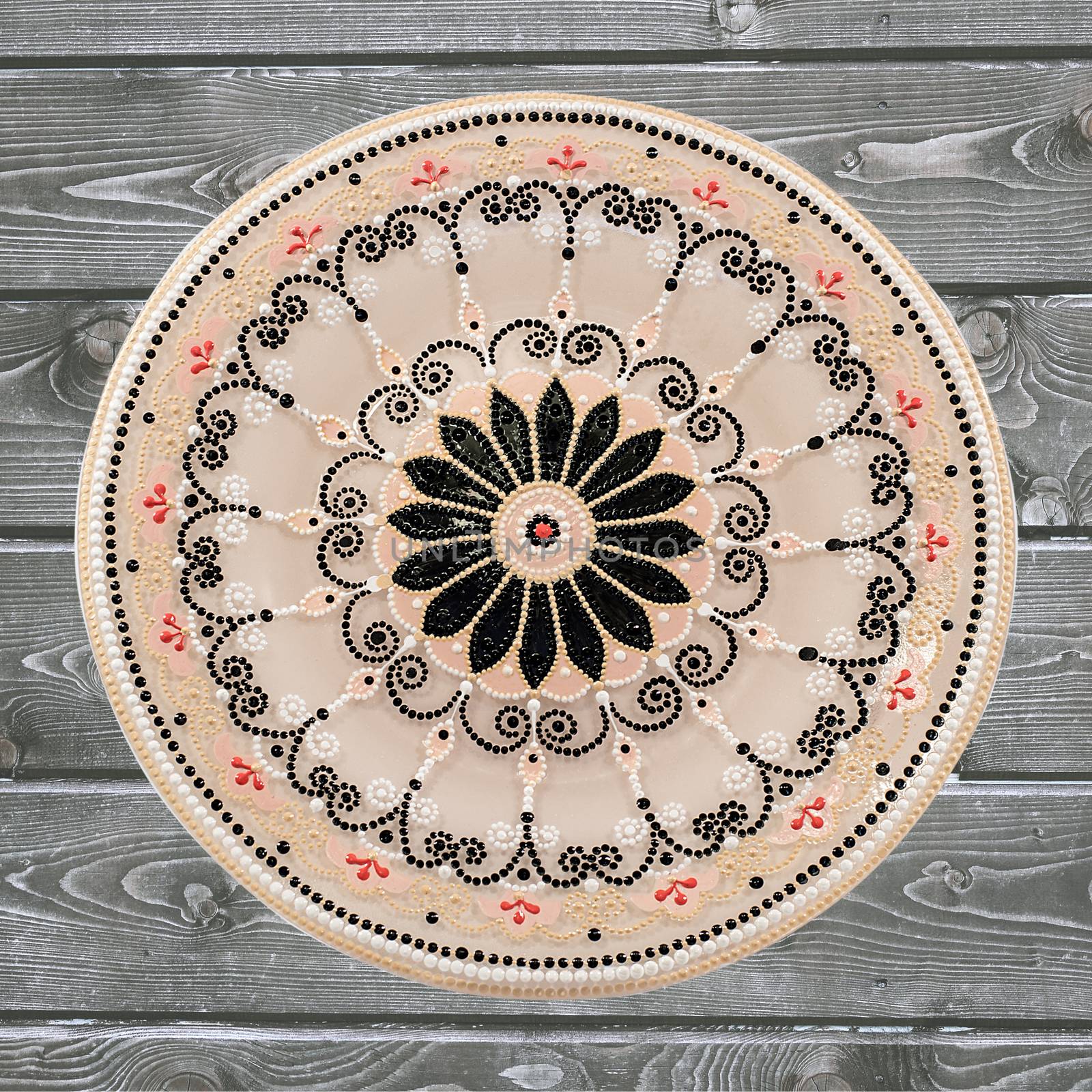 Decorative ceramic plate, hand painted dot pattern with acrylic paints on a gray wooden background. A square photo. Closeup