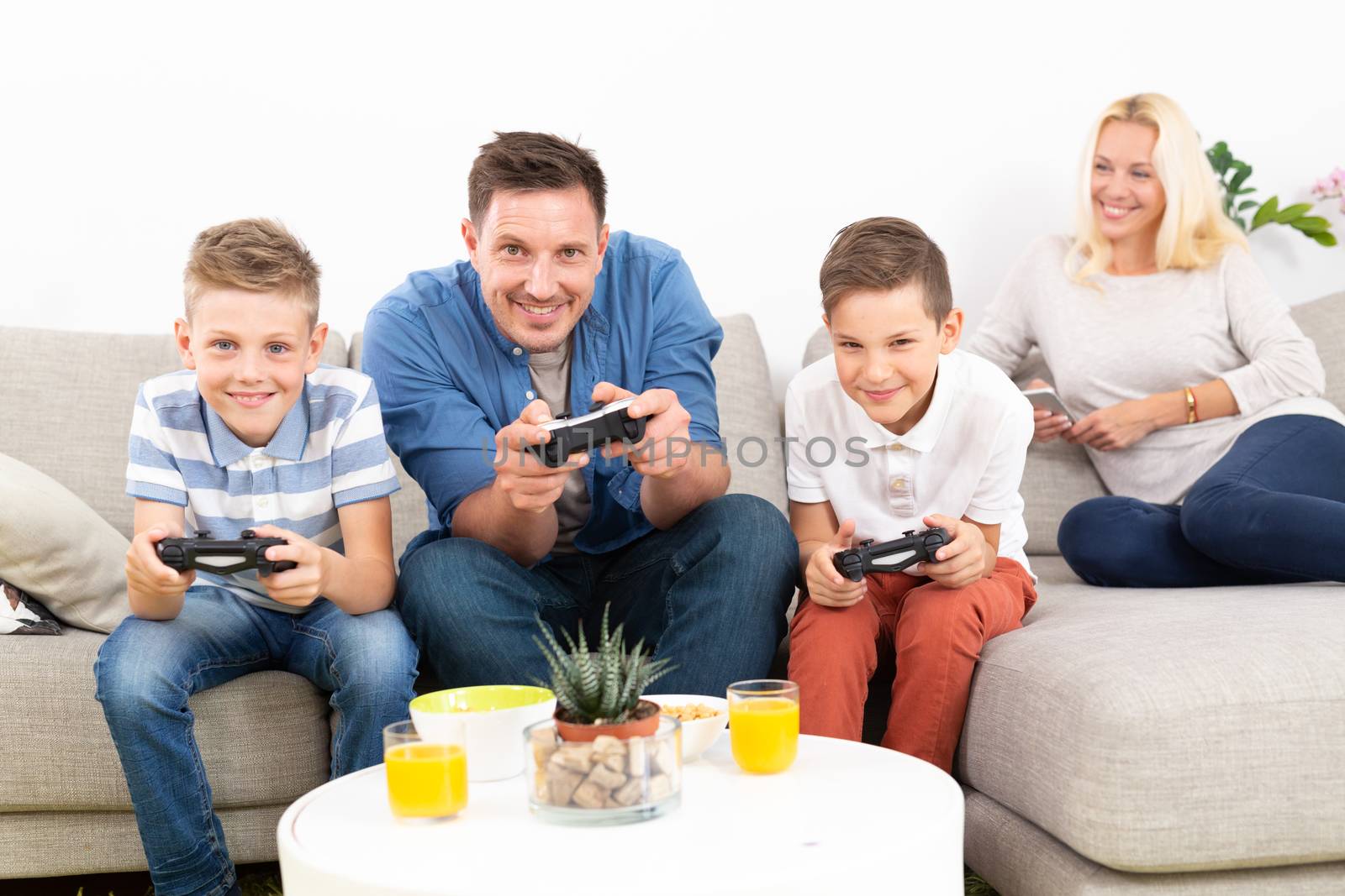 Happy young family playing videogame console on TV. Spending quality leisure time with children and family concept. Gaming consoles are generic and debranded.