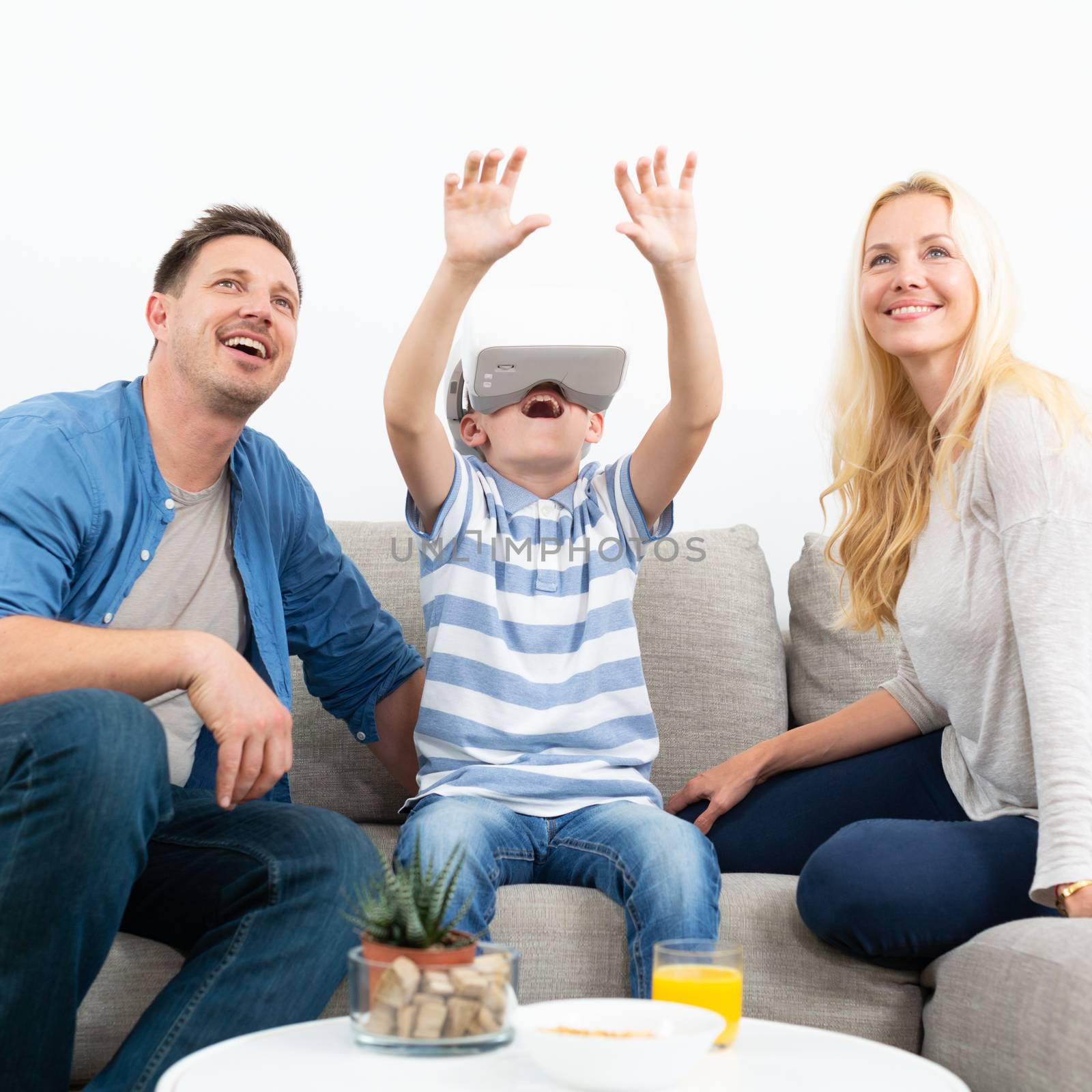 Happy caucasian family at home on living room sofa having fun playing games using virtual reality headset.