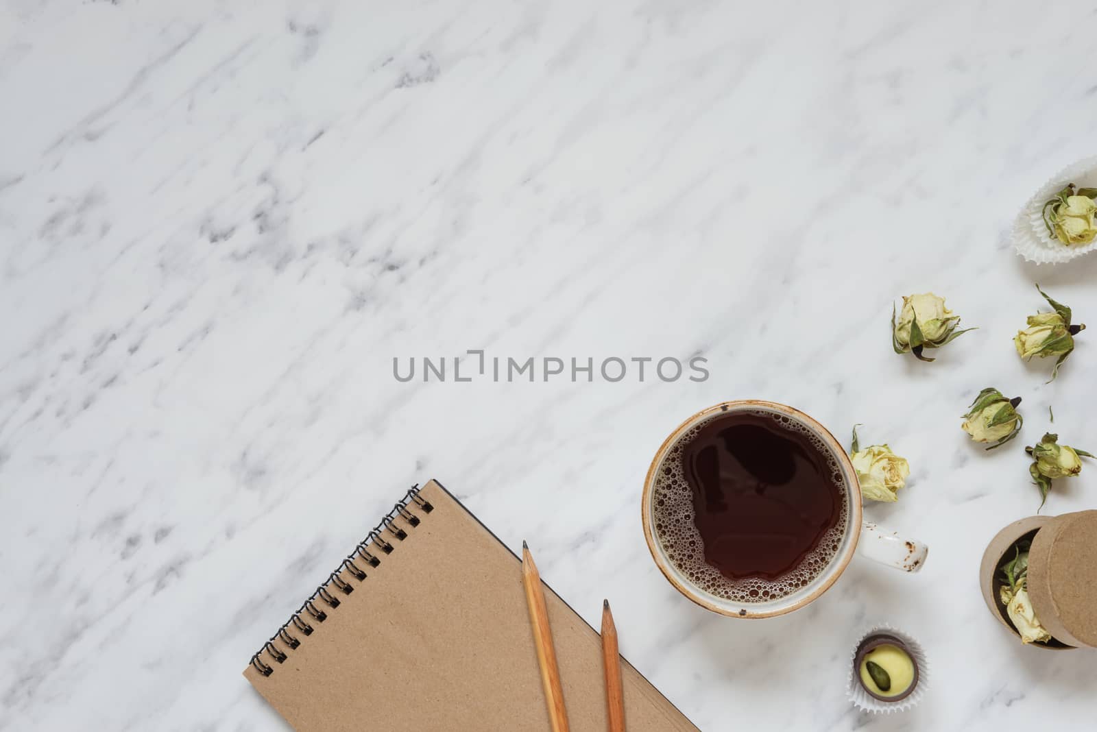 Morning composition with a cup of black coffee, chocolate candies and a notebook on a marble surface with space for text, top view