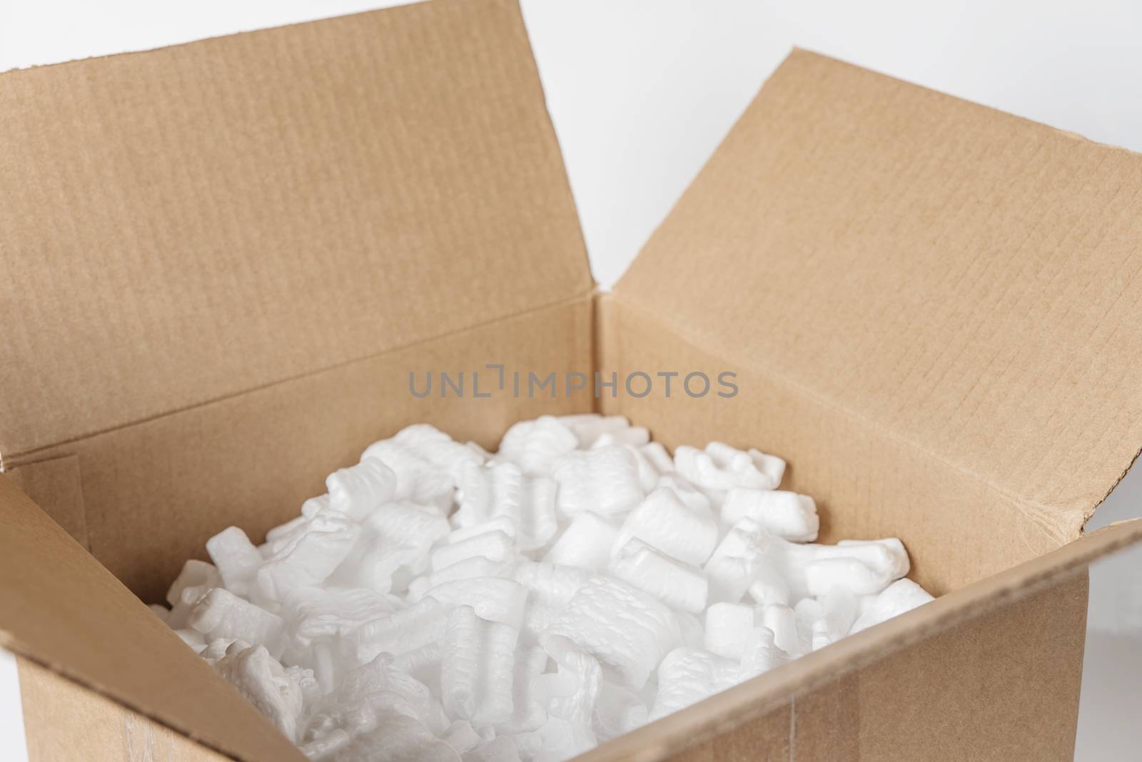 Opened cardboard box filled with polystyrene foam chips on a white background close-up