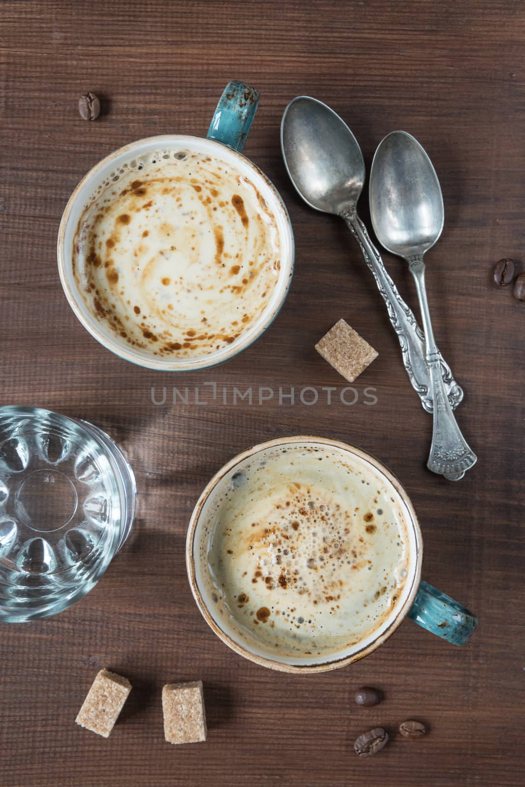 Two cups of coffee and are several pieces of sugar, glass of water and teaspoons; top view, flat lay