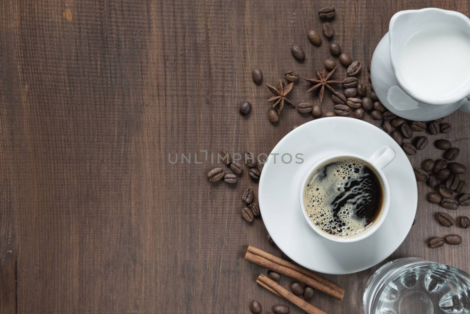 Cup of coffee, cream in a milk jug, glass of water and various spices on the wooden table with copy-space, top view