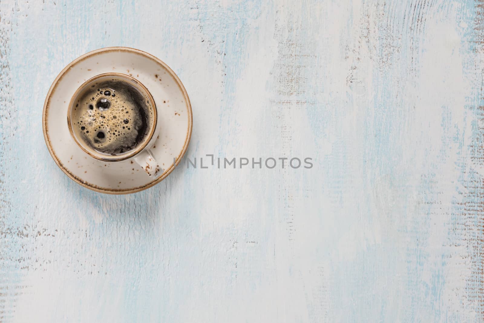Black coffee with crema in vintage porcelain cup on a light wooden background, with space for text, top view