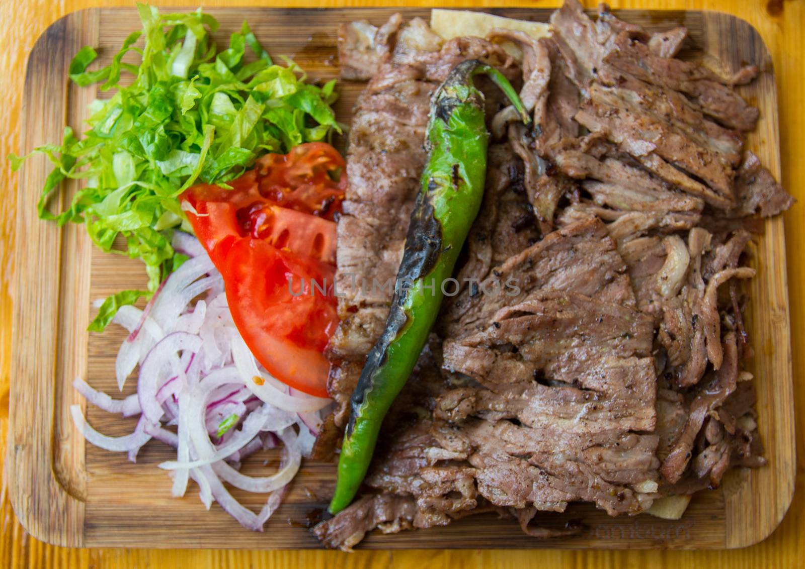 "Döner Kebab" is served with fresh greens on the board. 
famous turkish food. Döner kebab is a Turkish kebab, made of meat cooked on a vertical rotisserie.