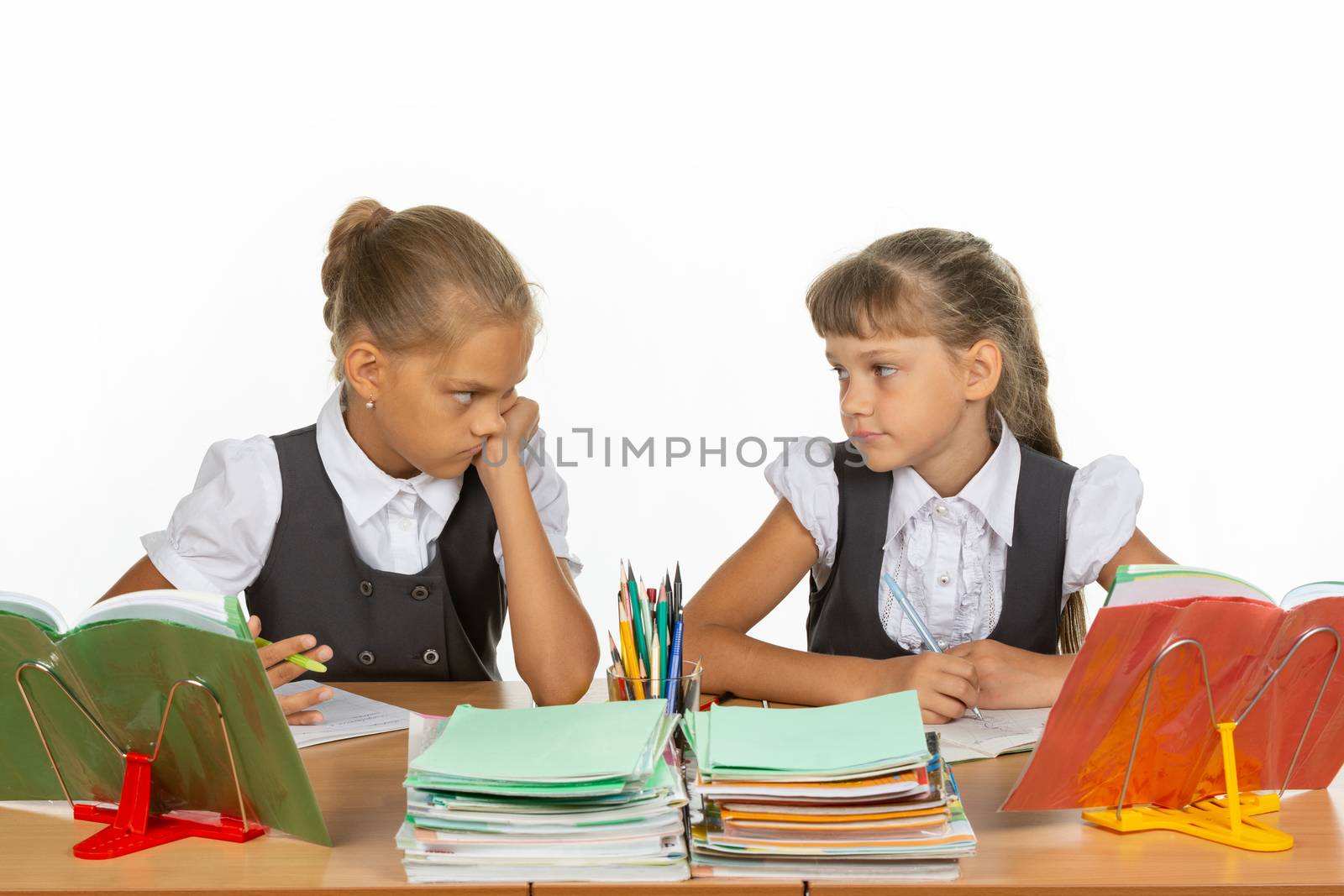 Two girls are sadly looking at each other, at a school desk
