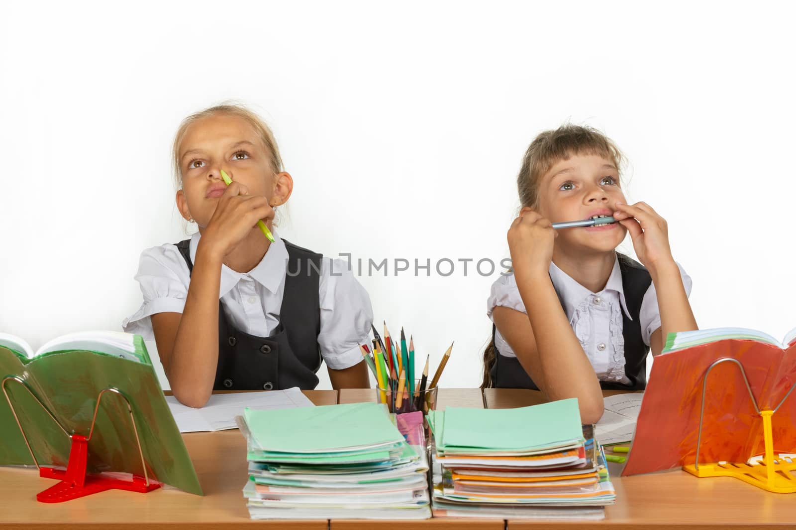 Two schoolgirls pensively and funny sit at the table and look up